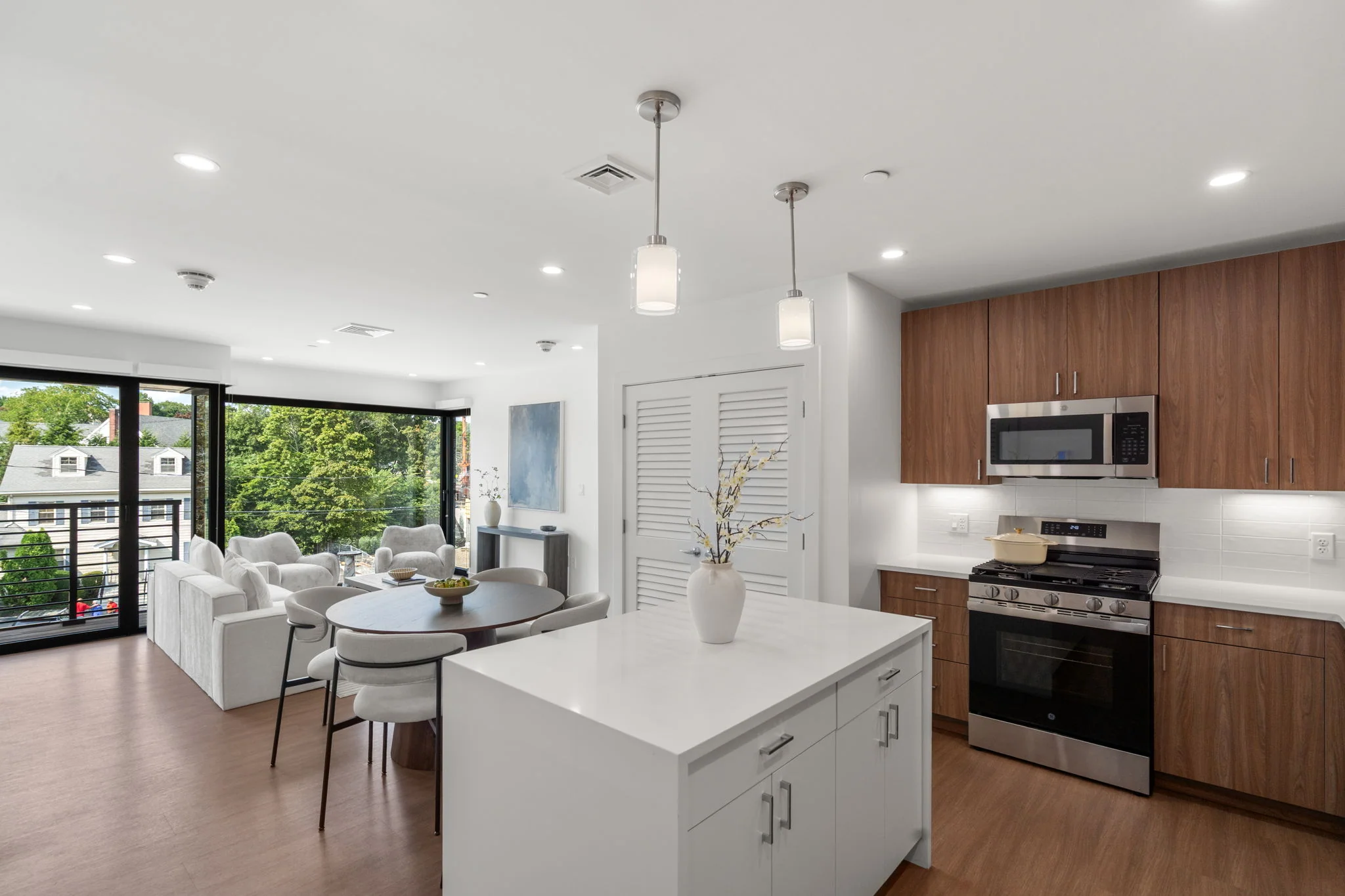 Open-plan kitchen with a white island, dining table, and living room beyond